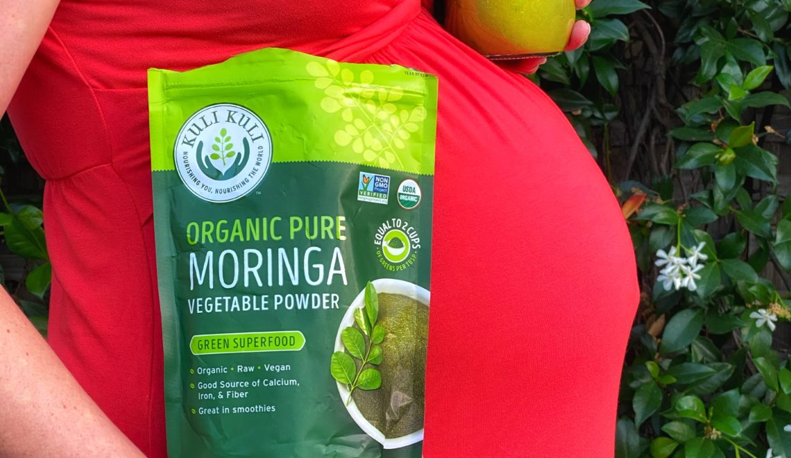 Pregnant woman in red dress with bag of moringa powder